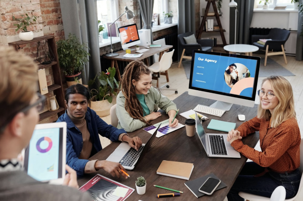 A team of people sitting around a desk with laptops.
